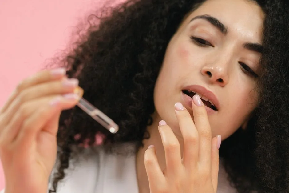 Close-up of a woman applying skincare serum with a pipette on pink background.